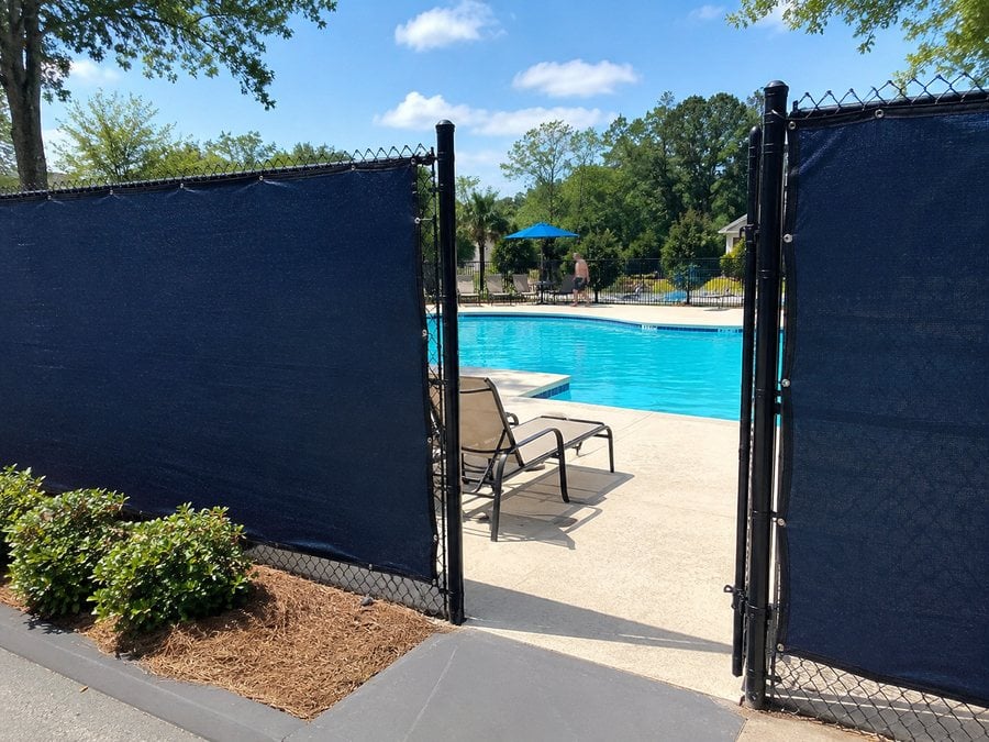 Pool enclosure fence wrapped in wind-blocking privacy mesh